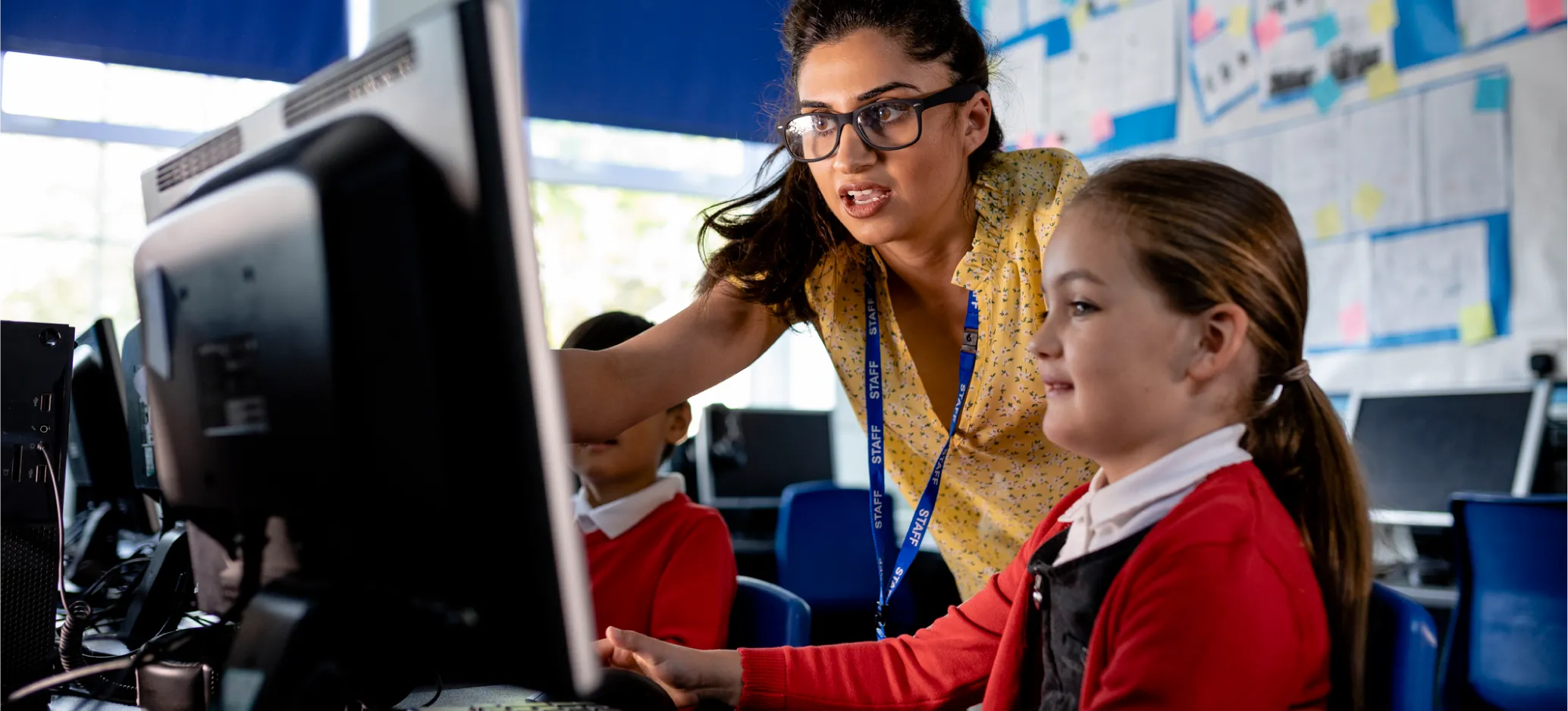 Teacher supporting a primary school pupil at a desktop computer