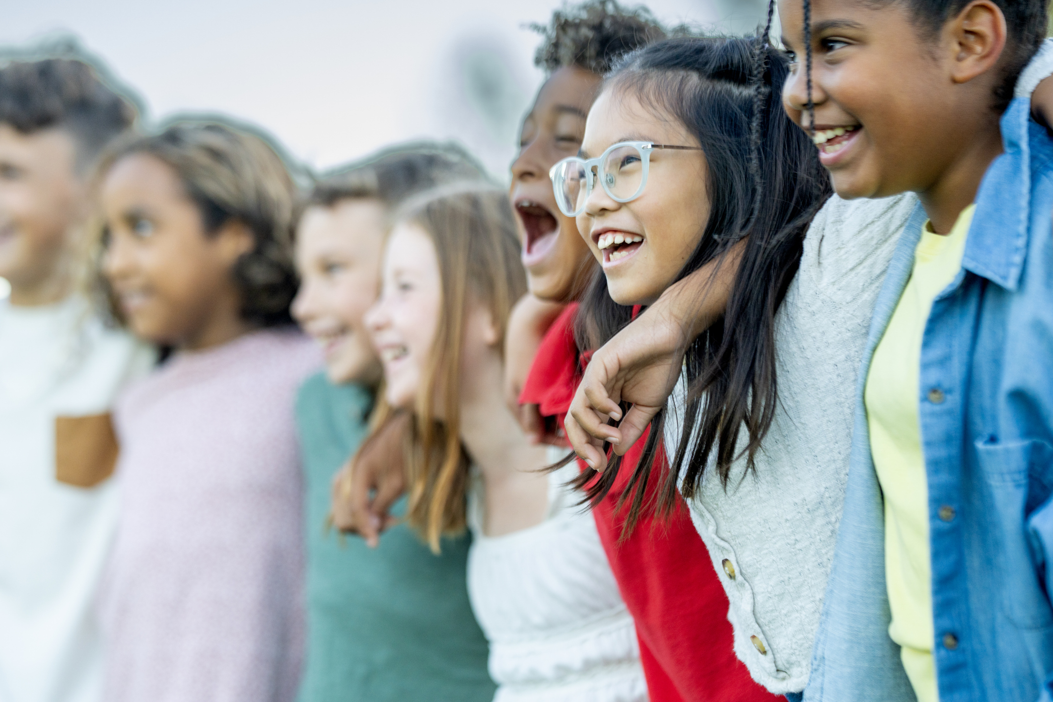 Diverse group of smiling children standing together with their arms around one another outdoors.