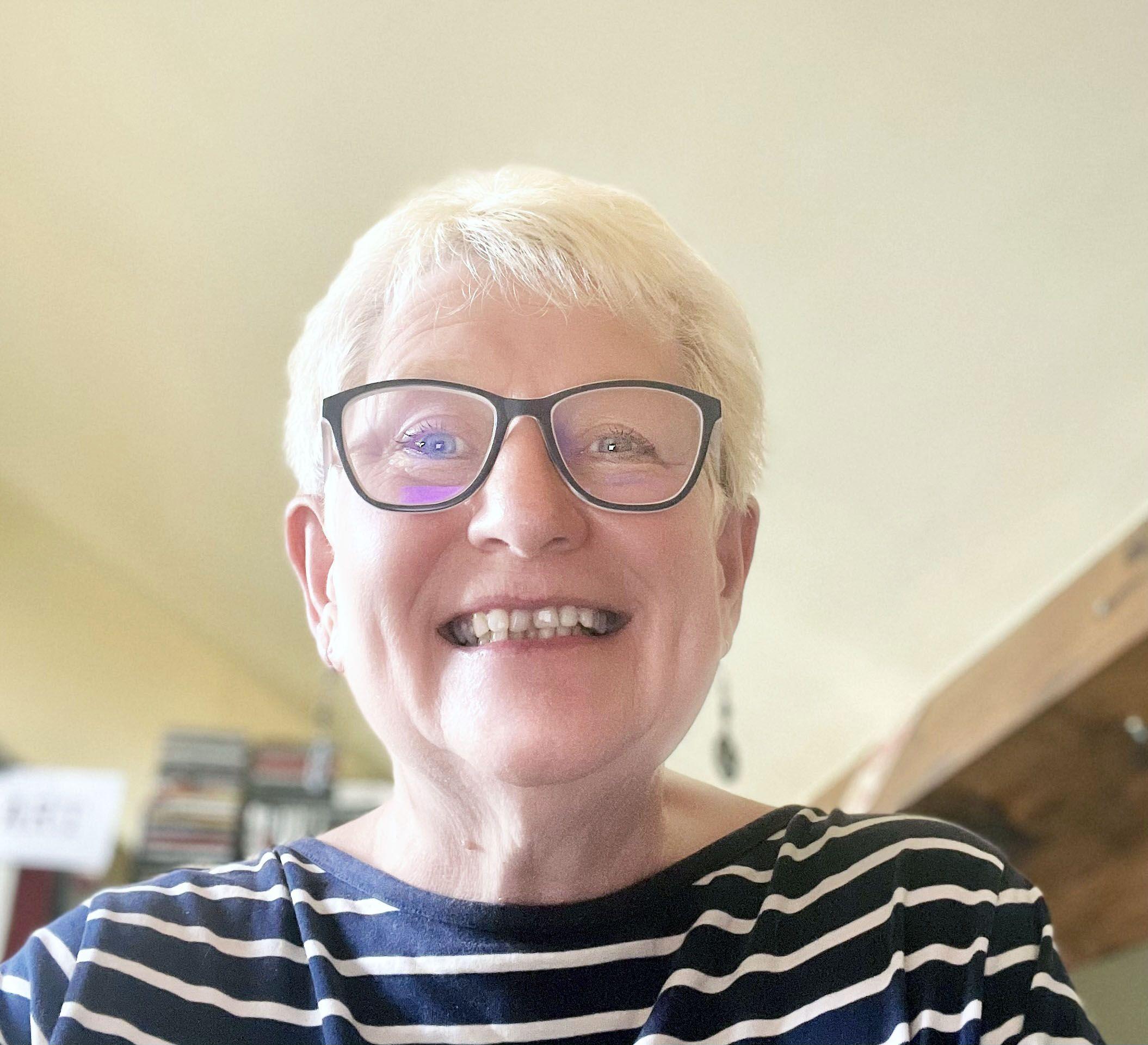 A smiling person wearing glasses and a navy striped top.