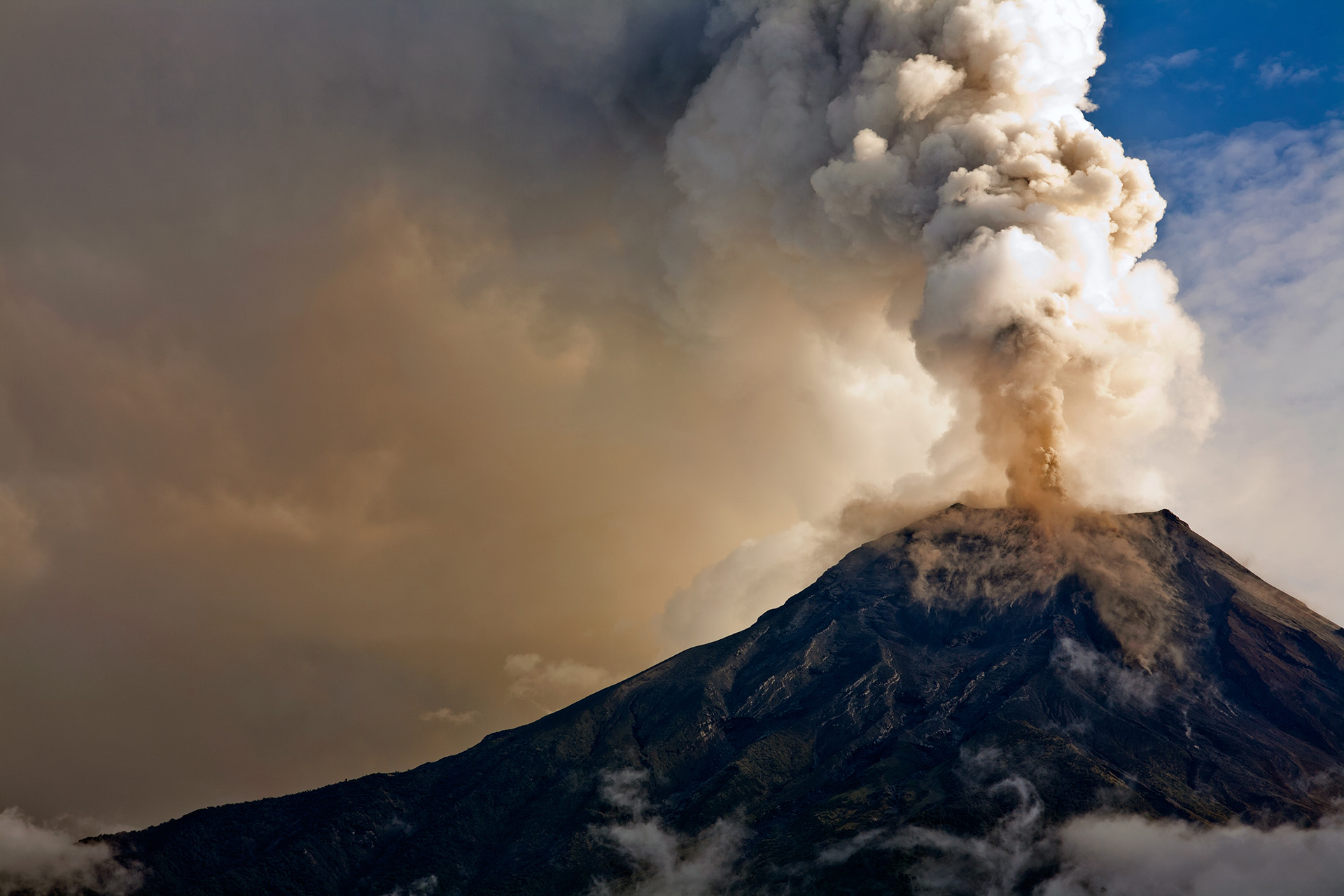 Volcano with gas erupting out the top and filling the sky.
