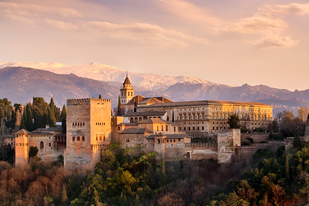 The Alhambra Palace in Granada, Spain, at sunset with the Sierra Nevada mountains in the background.