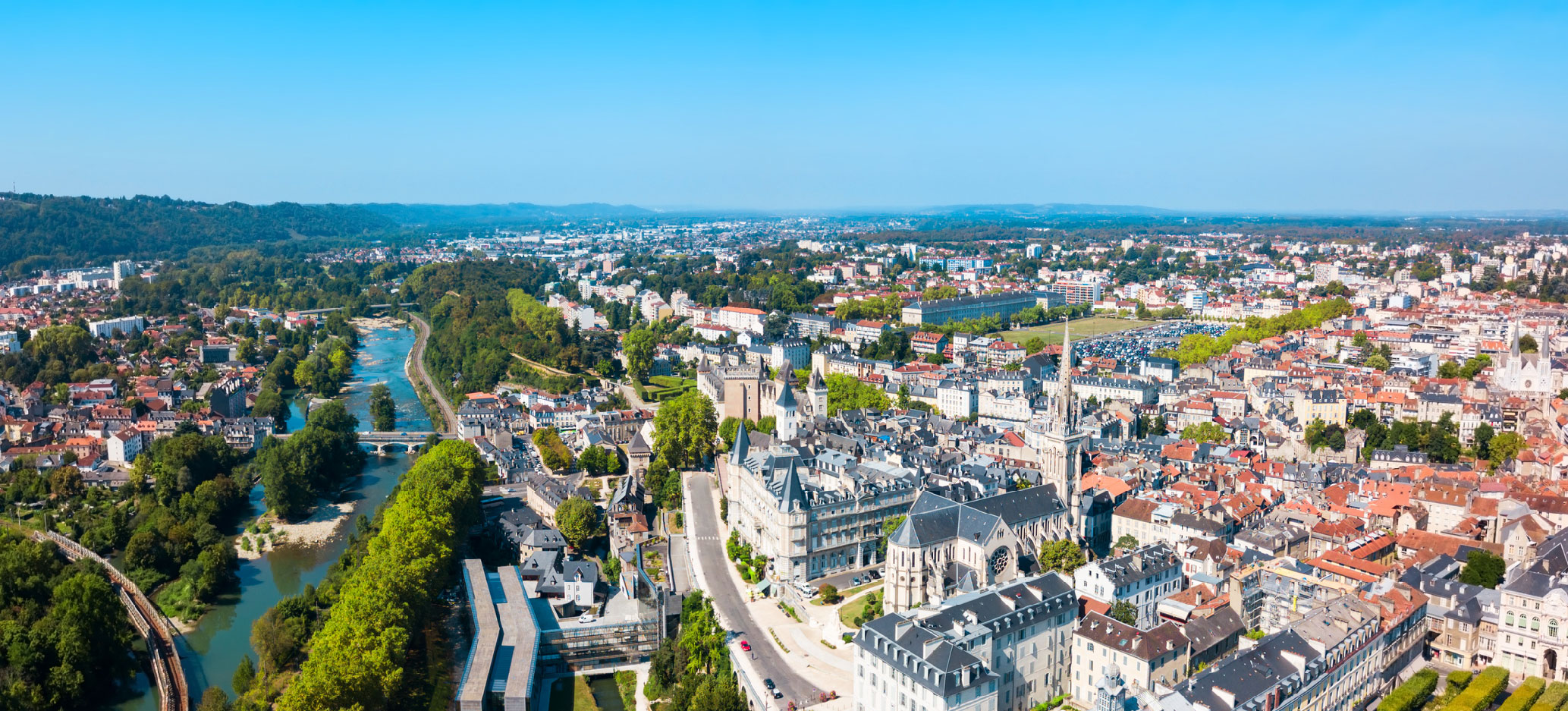An urban area with trees scattered throughout. There is a river running through the left of the city. The sky is clear and sunny.