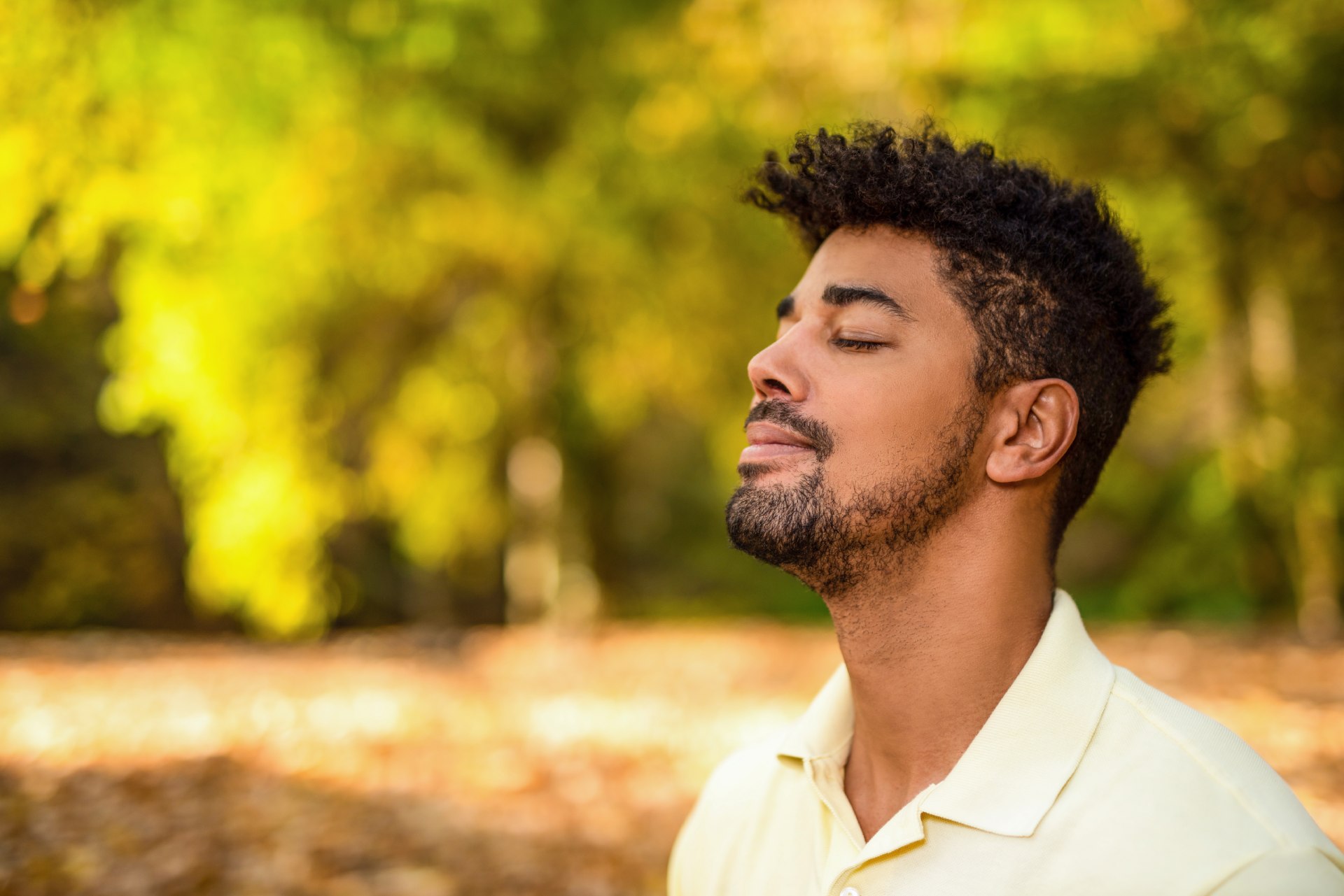 A man with closed eyes looks relaxed against a background of trees