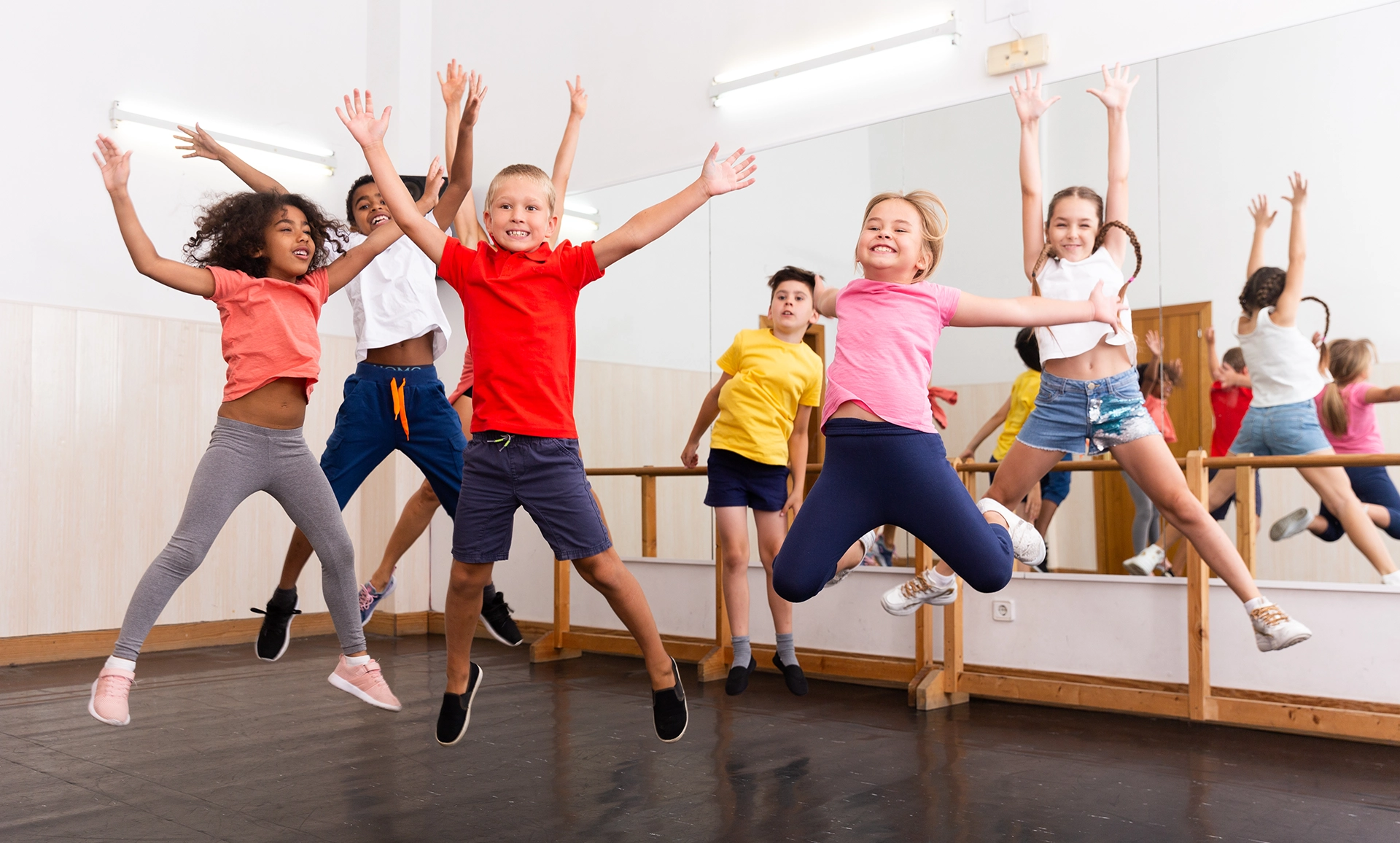 Children jumping with arms raised in a dance studio.