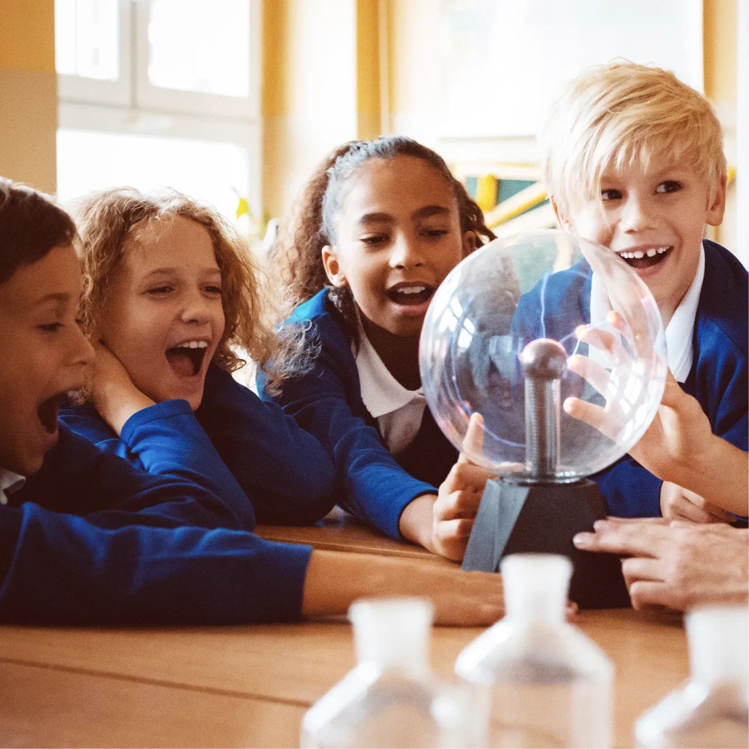 A group of schoolchildren exploring static electricity with a plasma ball in a classroom setting.