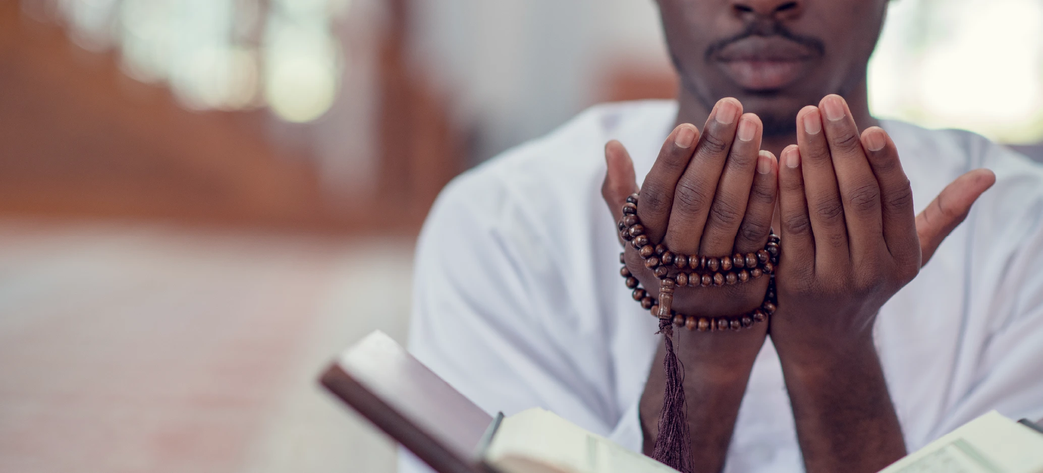 praying hands with rosary prayer beads over a bible