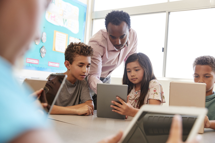 teacher showing primary school pupils how to work tablet device