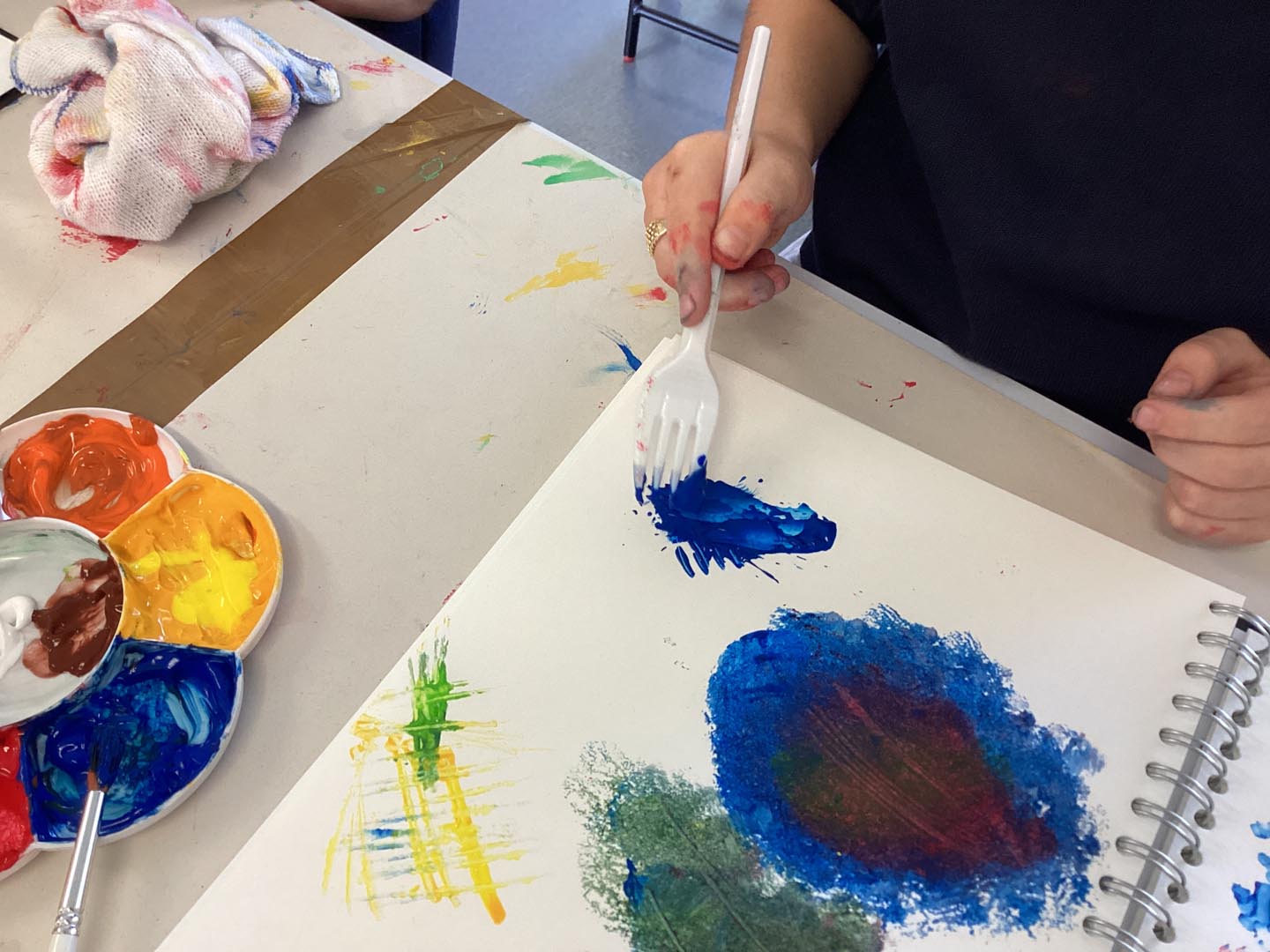 Child using a fork to scrape into paint on paper to create textures.