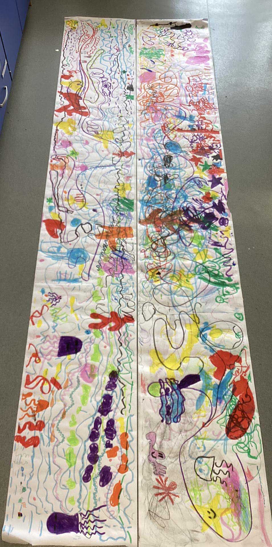 Long and large white piece of paper on the floor filled with children's doodles of lines and shapes inspired by listening to music