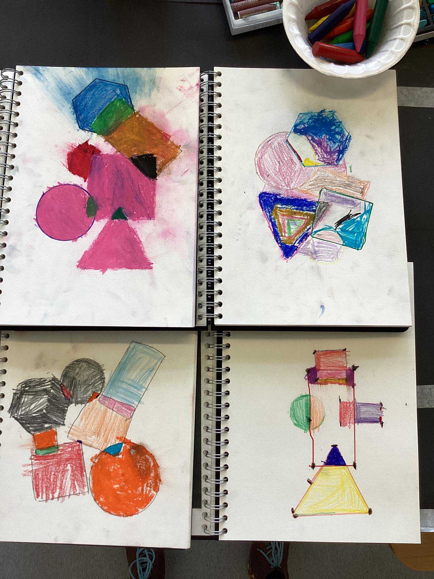 Selection of children's sketchbooks with shapes drawn overlapping and coloured in bright colours.