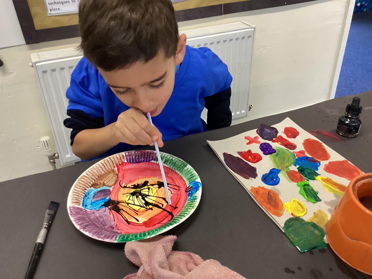 Children blowing through a straw to move paint over a paper paper plate art